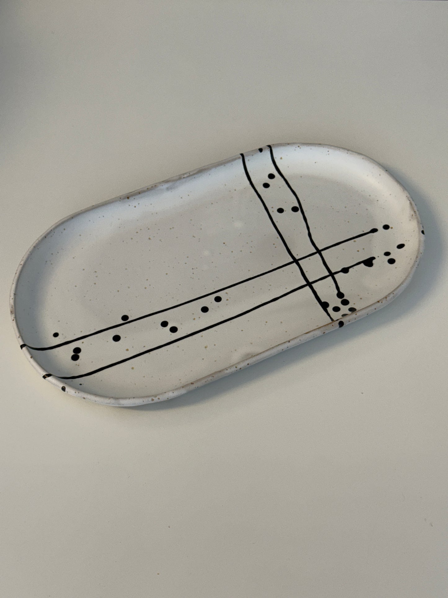 Es handelt sich um eine ovale Servierpatte in weiß matt mit schwarzem Muster auf spotted Clay.