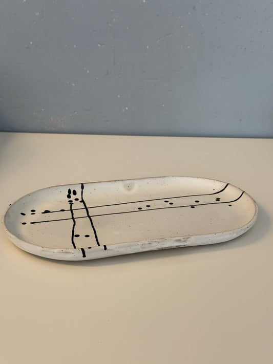 Es handelt sich um eine ovale Servierpatte in weiß matt mit schwarzem Muster auf spotted Clay.