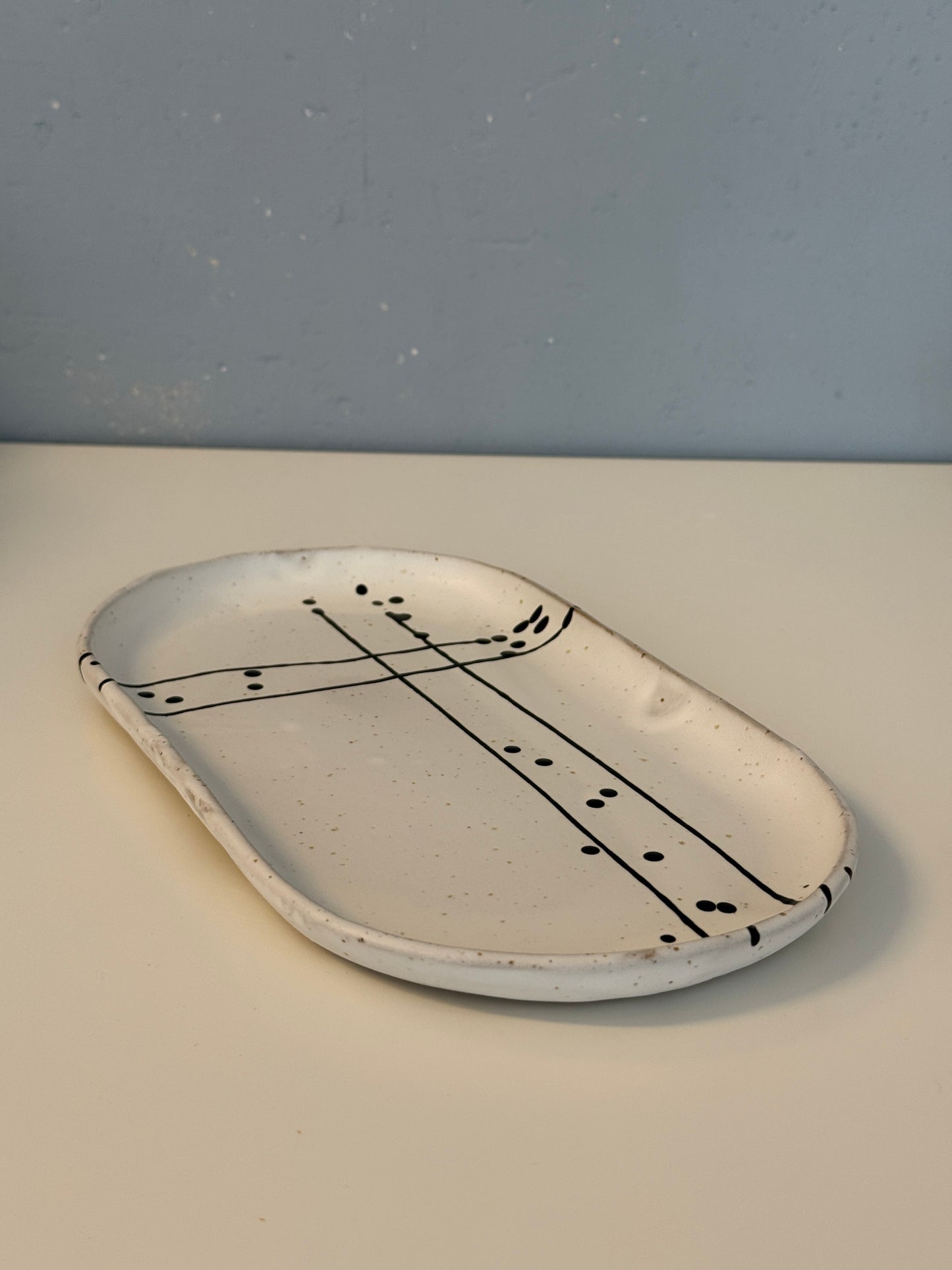 Es handelt sich um eine ovale Servierpatte in weiß matt mit schwarzem Muster auf spotted Clay.