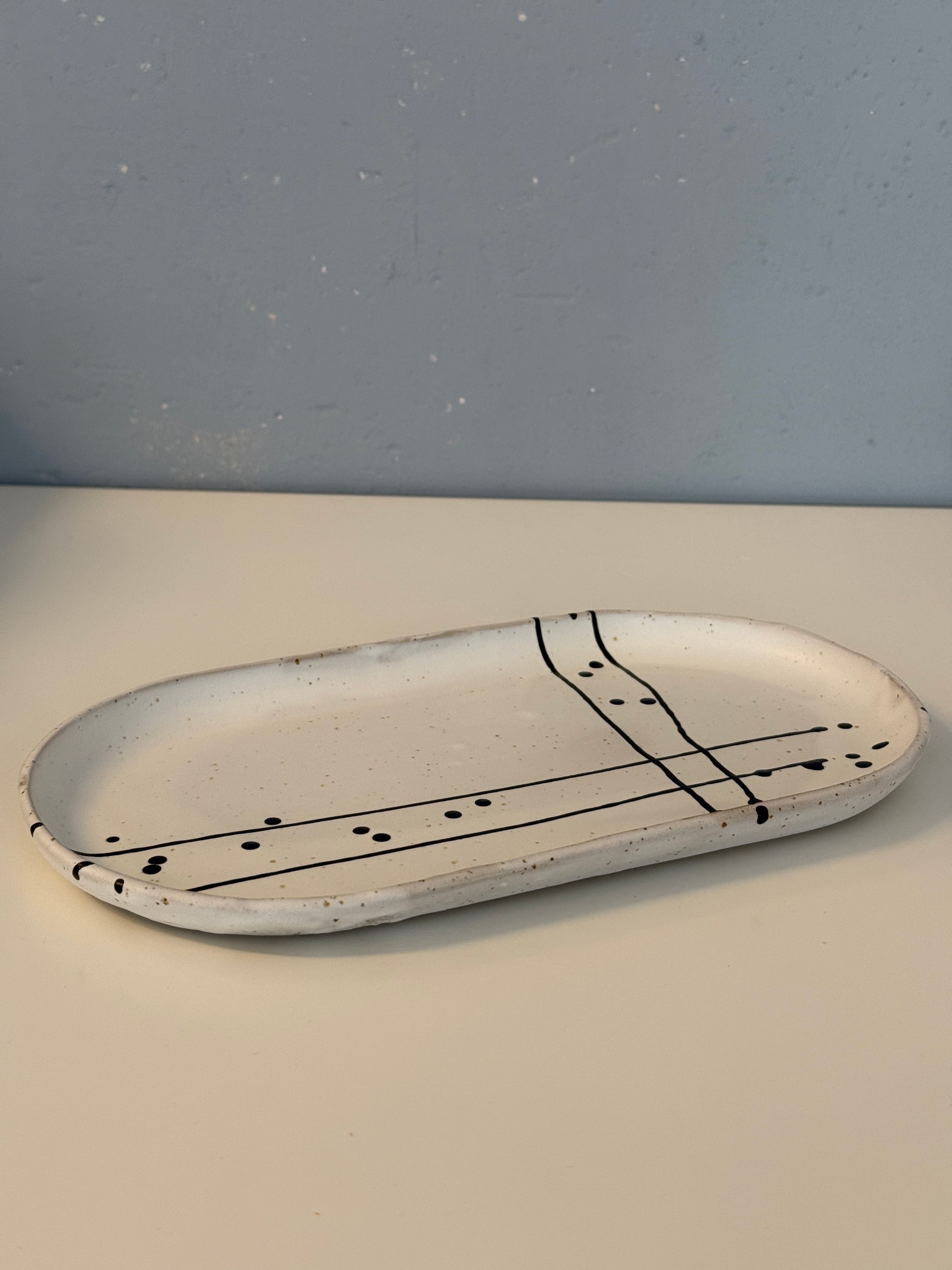 Es handelt sich um eine ovale Servierpatte in weiß matt mit schwarzem Muster auf spotted Clay.