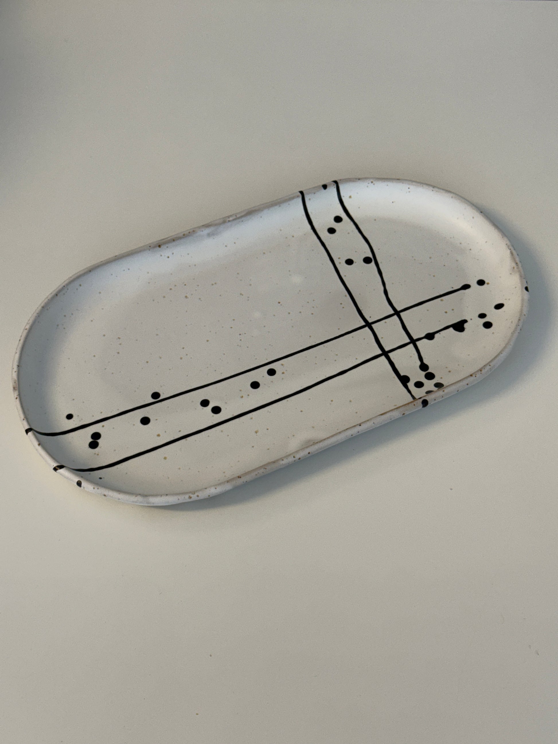 Es handelt sich um eine ovale Servierpatte in weiß matt mit schwarzem Muster auf spotted Clay.